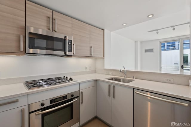 kitchen with stainless steel appliances, a sink, light countertops, track lighting, and recessed lighting