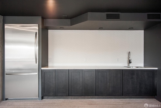 kitchen featuring stainless steel refrigerator, a sink, dark cabinets, and light countertops