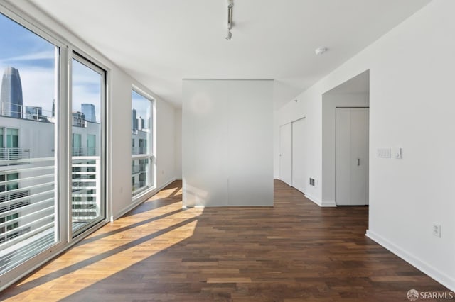 empty room with wood finished floors, baseboards, track lighting, and a view of city