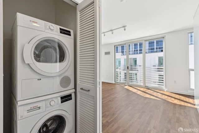 laundry room with stacked washer / drying machine, wood finished floors, rail lighting, and baseboards