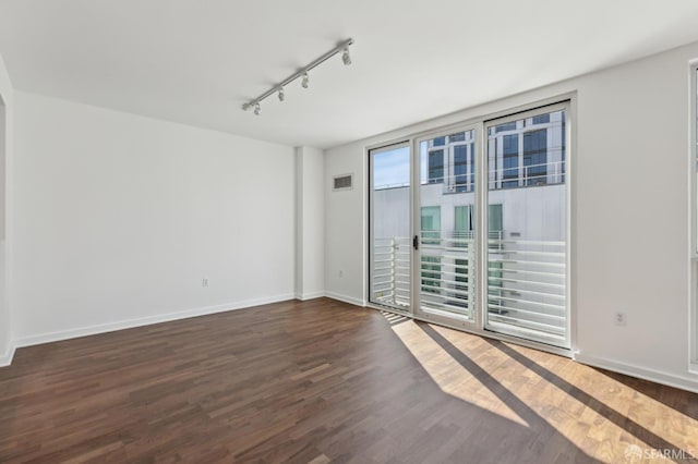 empty room featuring wood finished floors, rail lighting, and baseboards