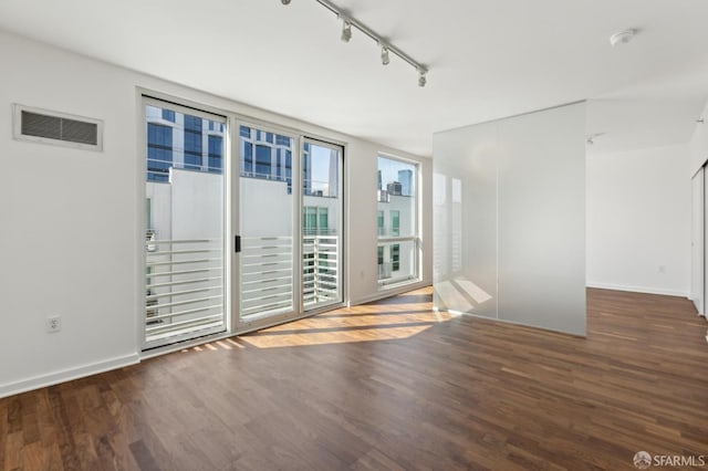 spare room featuring track lighting, wood finished floors, and baseboards