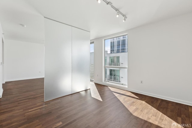 unfurnished room with rail lighting, wood finished floors, and baseboards