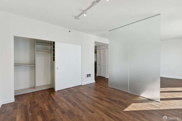 unfurnished bedroom featuring track lighting, wood finished floors, and baseboards