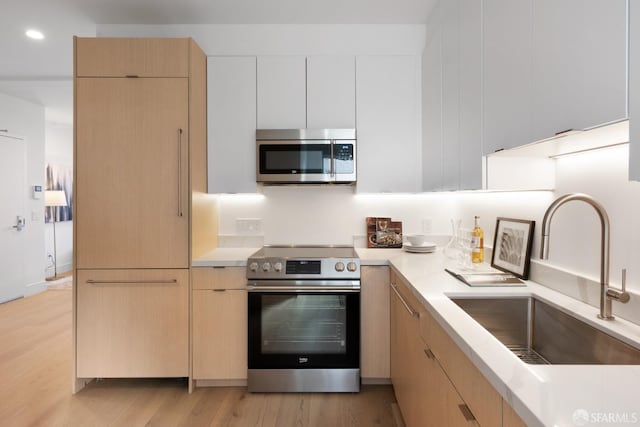 kitchen with sink, stainless steel appliances, light brown cabinets, and light hardwood / wood-style flooring