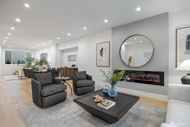 living area featuring wood finished floors, a glass covered fireplace, and recessed lighting