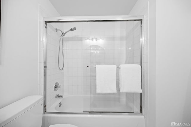 bathroom featuring toilet and shower / bath combination with glass door