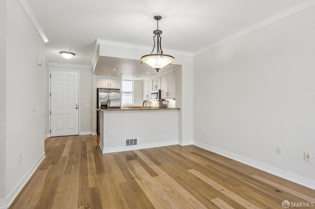 interior space featuring kitchen peninsula, crown molding, pendant lighting, white cabinets, and appliances with stainless steel finishes