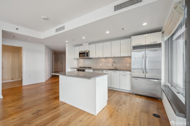 kitchen featuring white cabinets, a kitchen island, stainless steel appliances, sink, and light wood-type flooring