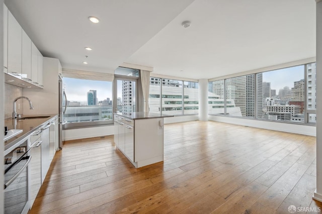 kitchen featuring a center island, appliances with stainless steel finishes, white cabinets, light wood-type flooring, and sink