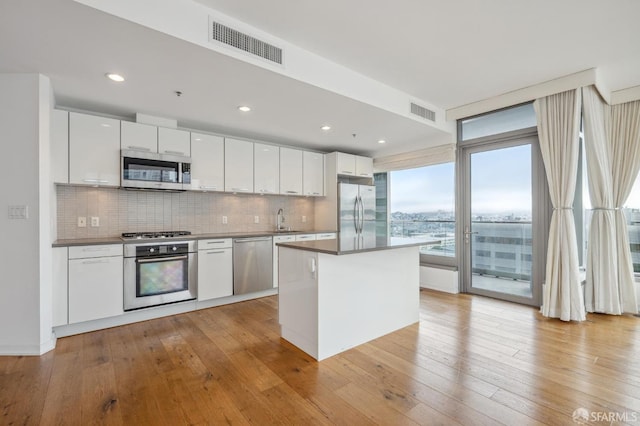 kitchen with appliances with stainless steel finishes, white cabinets, light wood-type flooring, tasteful backsplash, and a center island