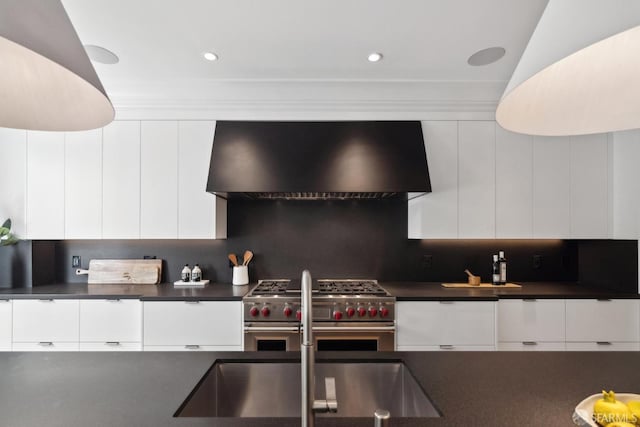kitchen with wall chimney range hood, high end stainless steel range, dark countertops, modern cabinets, and recessed lighting