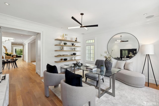living area with ornamental molding, ceiling fan, light wood finished floors, and baseboards