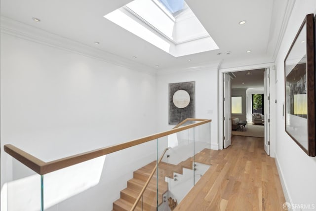 corridor featuring a skylight, light wood-style floors, crown molding, baseboards, and recessed lighting