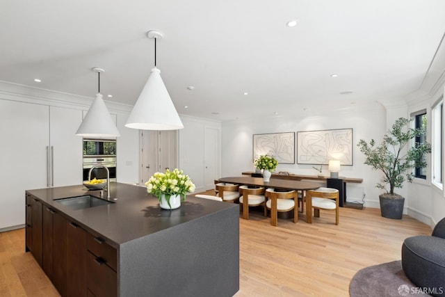 kitchen featuring oven, dark countertops, a sink, built in microwave, and light wood finished floors