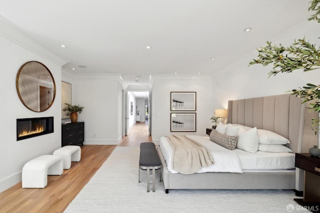 bedroom featuring wood finished floors, a glass covered fireplace, recessed lighting, ornamental molding, and baseboards