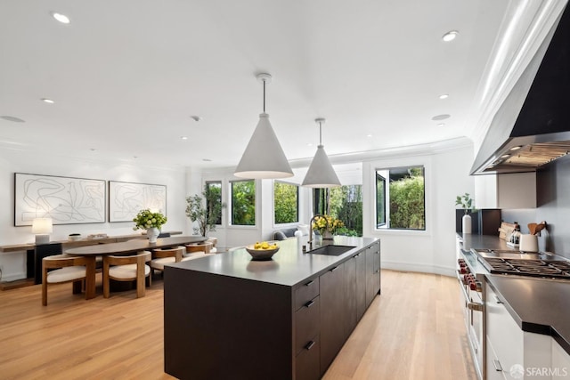 kitchen featuring wall chimney exhaust hood, a sink, light wood finished floors, stainless steel range, and dark countertops