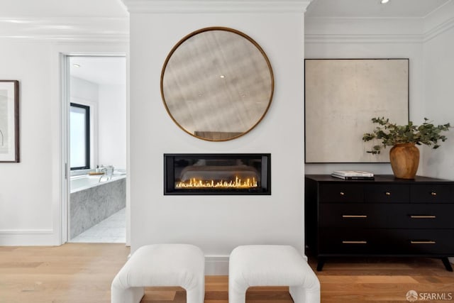 living area with crown molding, light wood finished floors, and a glass covered fireplace