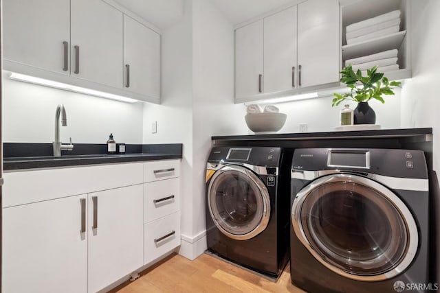 clothes washing area featuring washing machine and clothes dryer, light wood-style flooring, and cabinet space