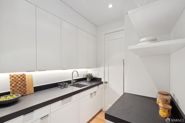 kitchen with a sink, white cabinets, modern cabinets, dark countertops, and recessed lighting