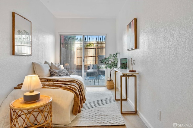 bedroom featuring access to exterior, light wood-type flooring, a textured wall, and baseboards