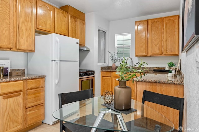 kitchen with under cabinet range hood, stainless steel range with gas stovetop, dark stone countertops, and freestanding refrigerator