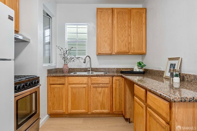 kitchen with freestanding refrigerator, stainless steel gas stove, a sink, dark stone counters, and extractor fan