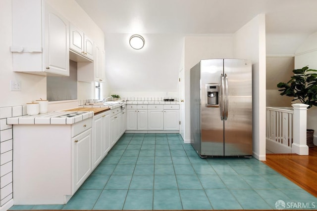 kitchen featuring lofted ceiling, light tile patterned floors, white cabinets, tile counters, and stainless steel fridge