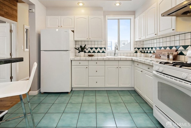 kitchen with white appliances, white cabinets, tile countertops, under cabinet range hood, and a sink