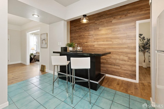 bar featuring freestanding refrigerator, wood walls, a dry bar, and wood finished floors