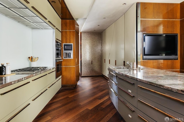 kitchen with stainless steel appliances, dark wood-style flooring, a sink, gray cabinets, and light stone countertops