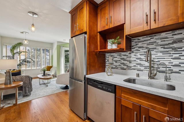 kitchen with a sink, appliances with stainless steel finishes, light wood finished floors, decorative backsplash, and light stone countertops