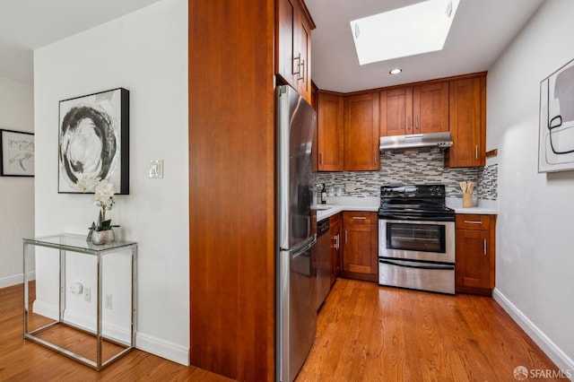 kitchen with under cabinet range hood, light countertops, decorative backsplash, a skylight, and stainless steel appliances