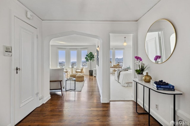 foyer with arched walkways, ornamental molding, dark wood-style flooring, and baseboards