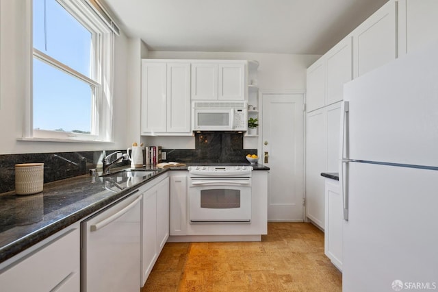 kitchen featuring white appliances, a sink, white cabinetry, backsplash, and dark stone counters