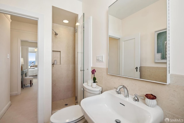 bathroom featuring a stall shower, toilet, a wainscoted wall, a sink, and tile walls