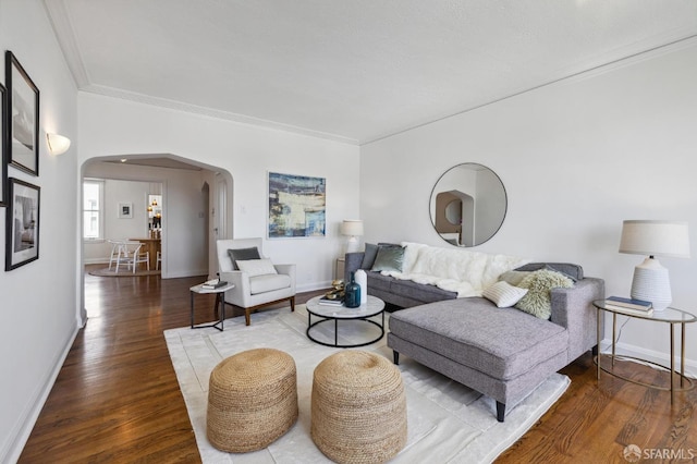 living area featuring arched walkways, crown molding, baseboards, and wood finished floors