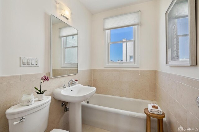 bathroom with toilet, a wainscoted wall, tile walls, and a bath