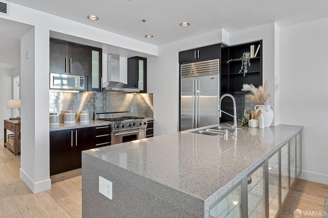 kitchen with wall chimney range hood, modern cabinets, high quality appliances, and a sink