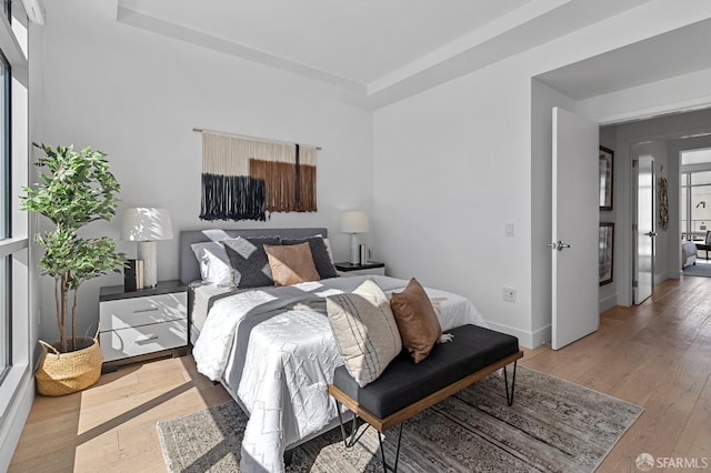 bedroom featuring light wood-type flooring, baseboards, and a raised ceiling