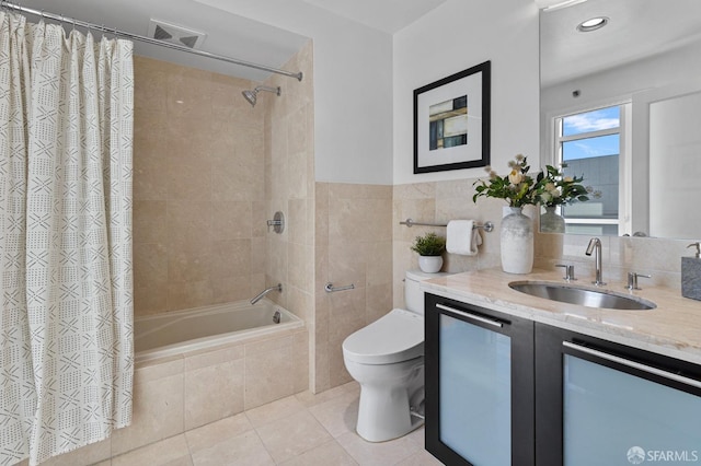 full bathroom with tile patterned flooring, toilet, tiled shower / bath combo, vanity, and tile walls