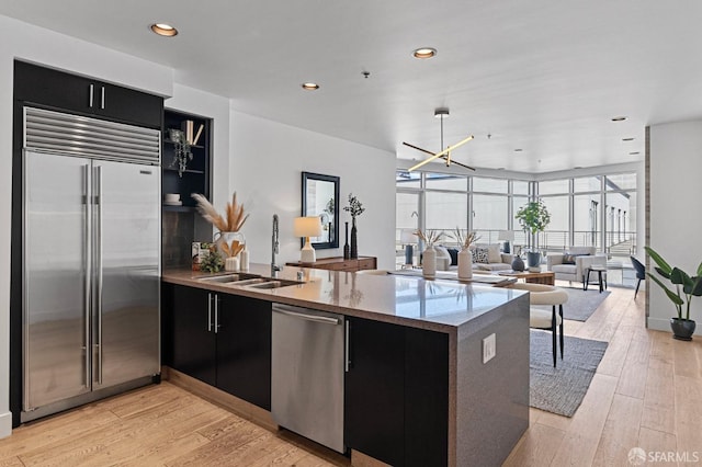 kitchen featuring dark cabinets, a peninsula, stainless steel appliances, light wood-type flooring, and a sink