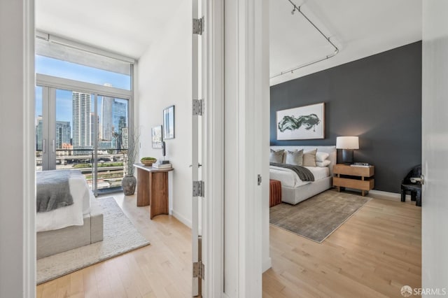 bedroom with light wood-type flooring, a wall of windows, and track lighting