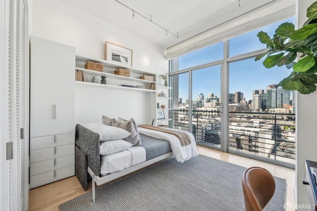 bedroom featuring light hardwood / wood-style floors, access to exterior, track lighting, and floor to ceiling windows