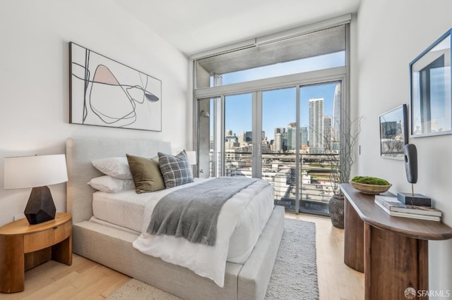 bedroom with light hardwood / wood-style floors, access to exterior, and a wall of windows