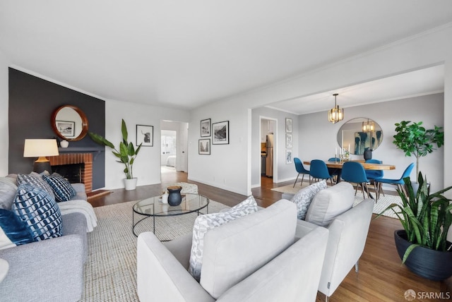 living area featuring baseboards, a chandelier, ornamental molding, a fireplace, and wood finished floors