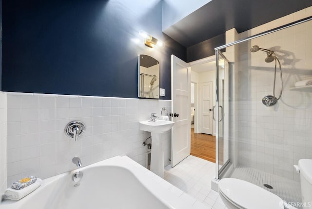 bathroom featuring a wainscoted wall, toilet, tile walls, and a stall shower