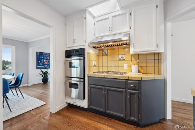 kitchen featuring stainless steel appliances, tasteful backsplash, extractor fan, and white cabinetry