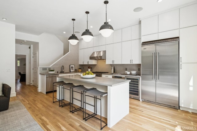 kitchen with a kitchen bar, light wood-type flooring, beverage cooler, under cabinet range hood, and stainless steel appliances