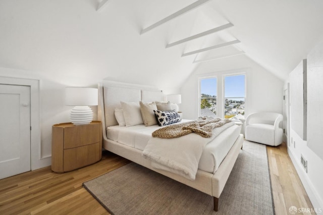bedroom with light wood-type flooring, visible vents, and vaulted ceiling with beams